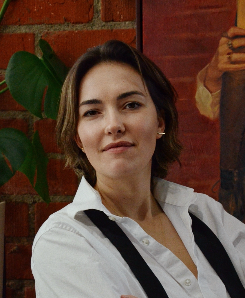Woman wearing a white shirt with a tie and cropped hair against a brick wall.